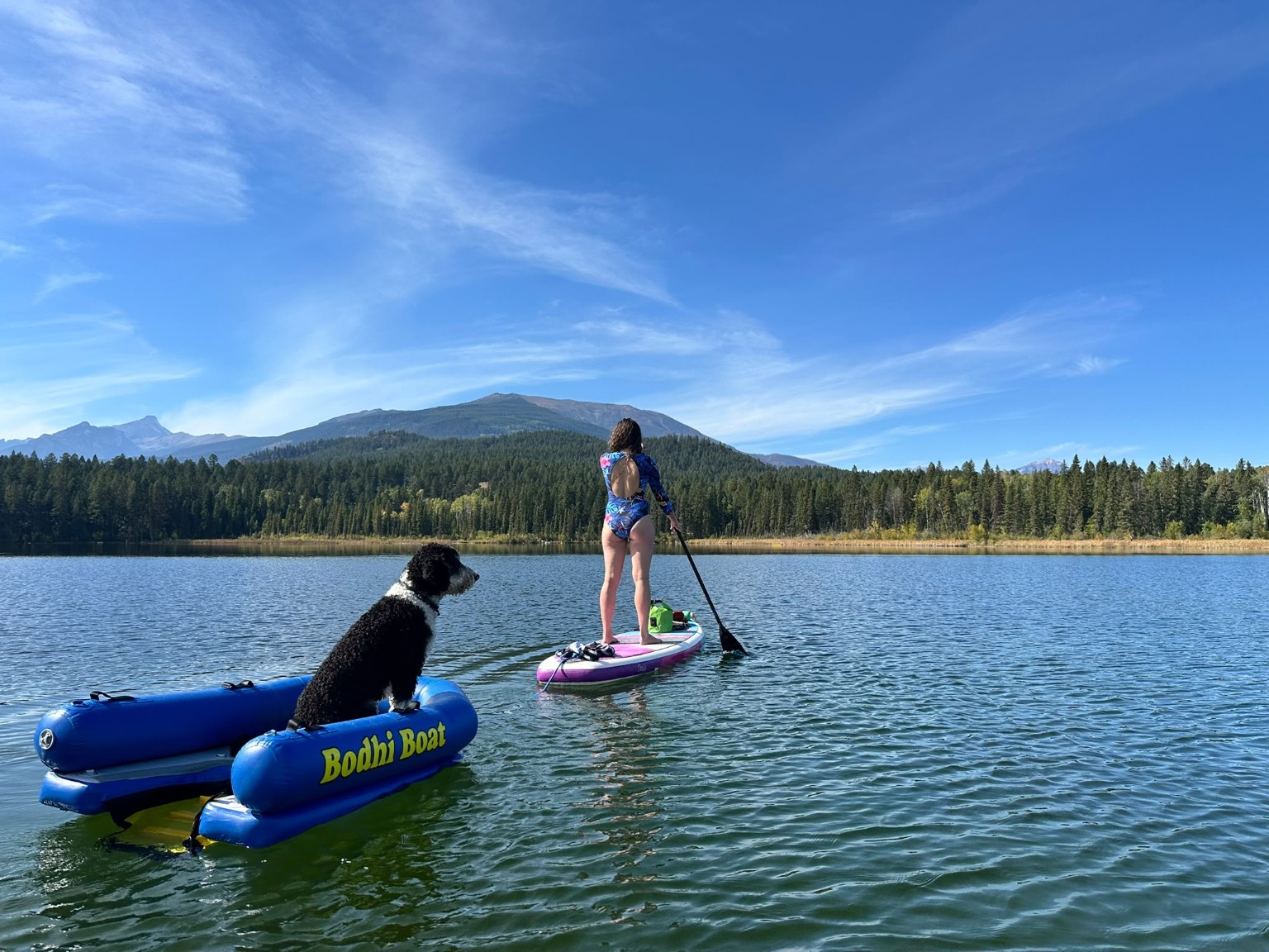 Bodhi riding in the Bodhi Boat while being towed behind a woman paddleboarding